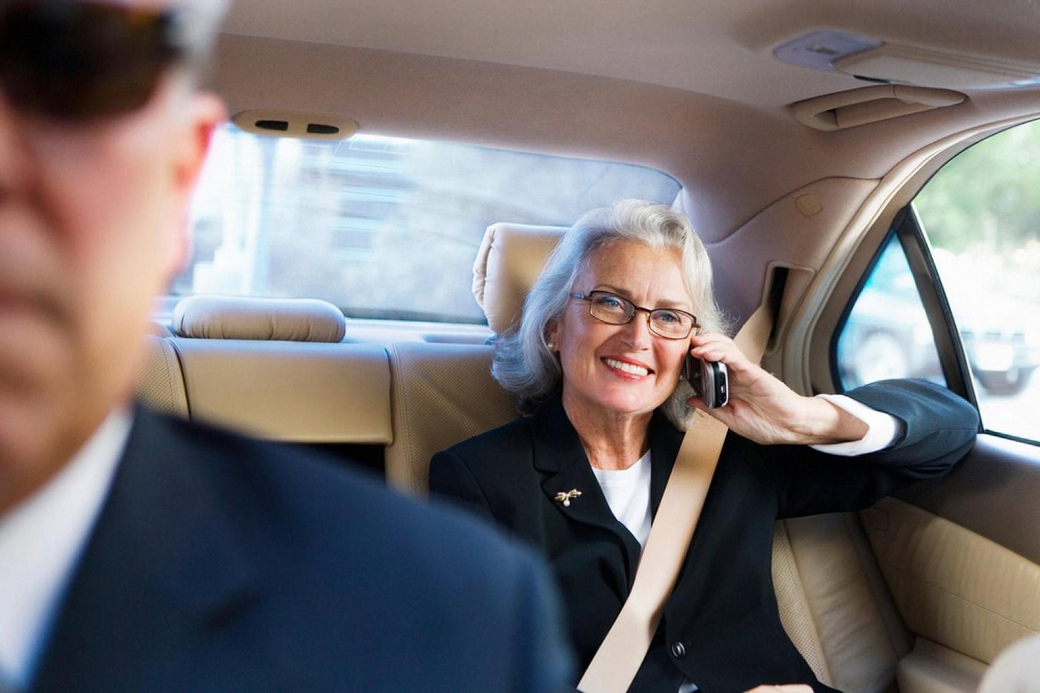 Senior executive on a call in the rear seat of a luxury chauffeur-driven vehicle with the driver visible in the foreground