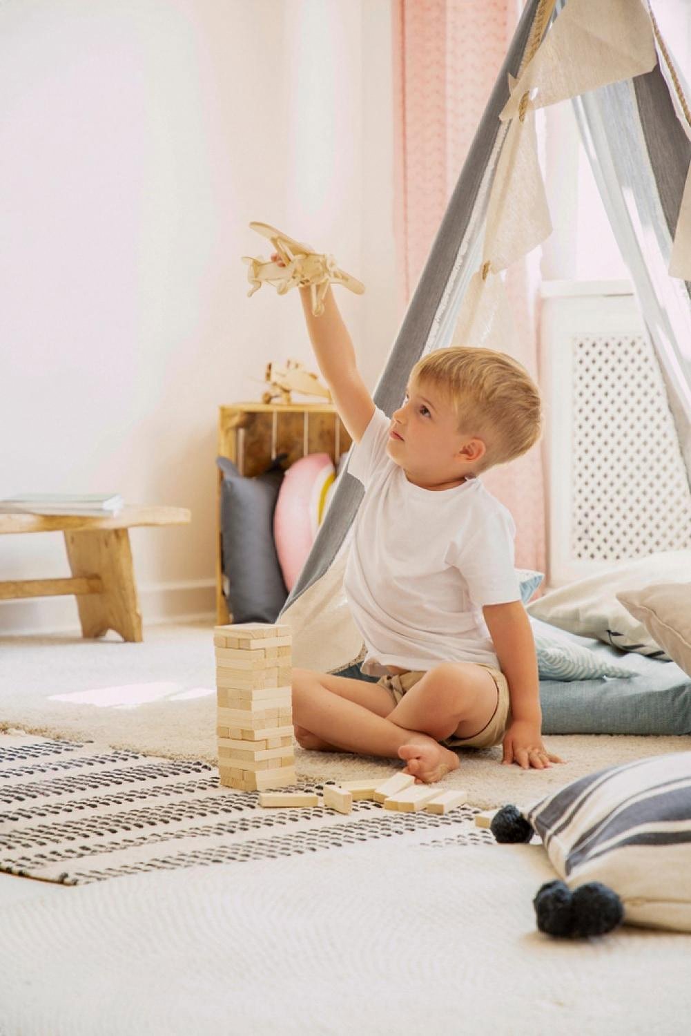 Young child playing with wooden building blocks and a wooden toy plane inside a tepee