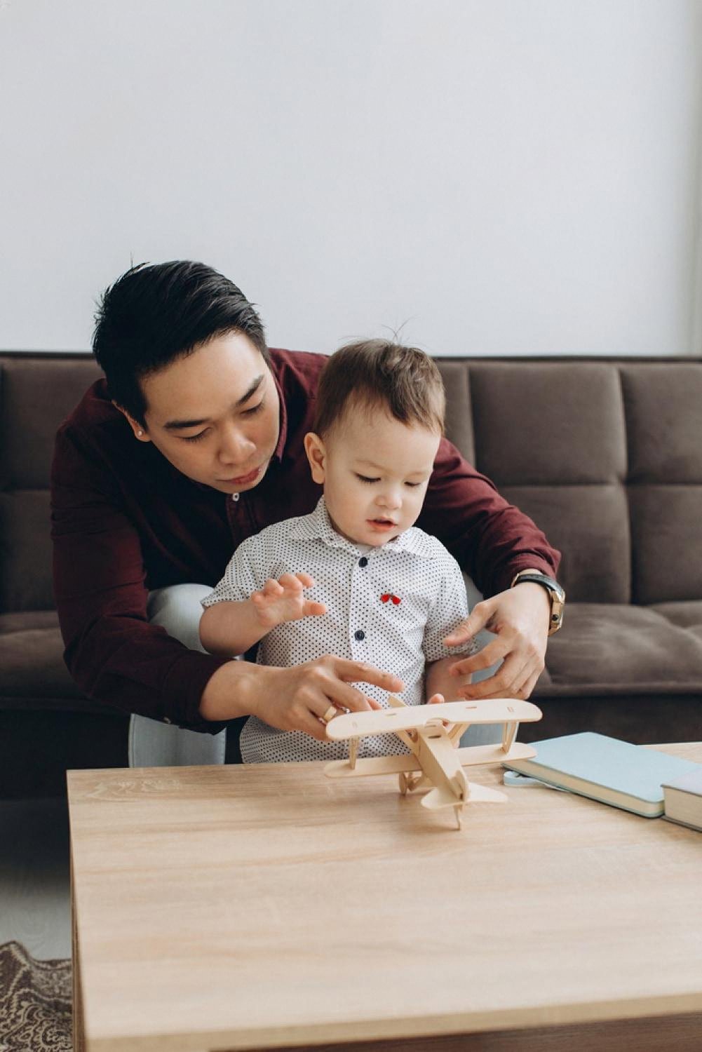 Father helping his toddler assemble a wooden toy aeroplane on a coffee table